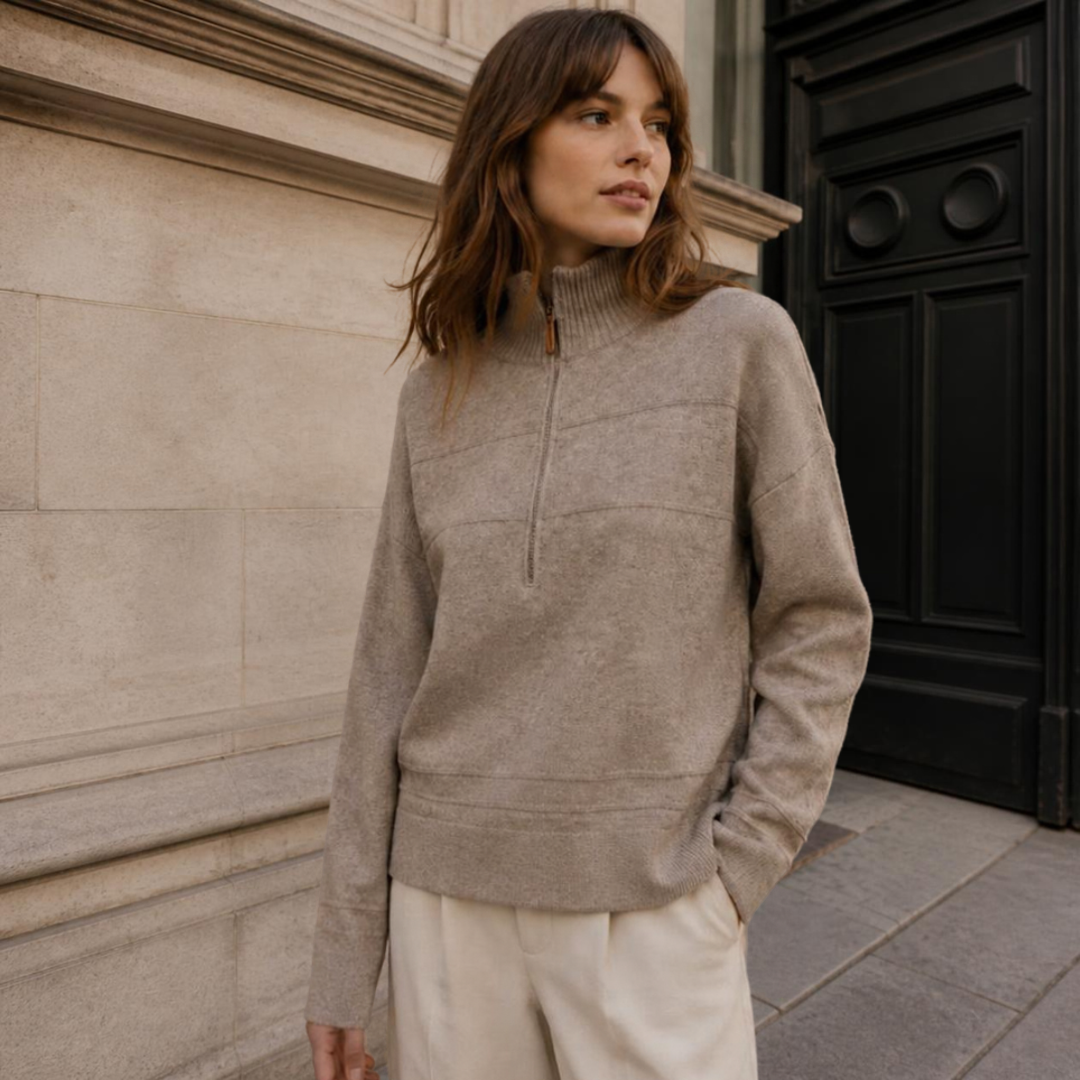 Model wearing KIDDING high-neck zip-up trucker sweater in sandy colour with ribbed collar, cuffs, and hem, paired with cream trousers