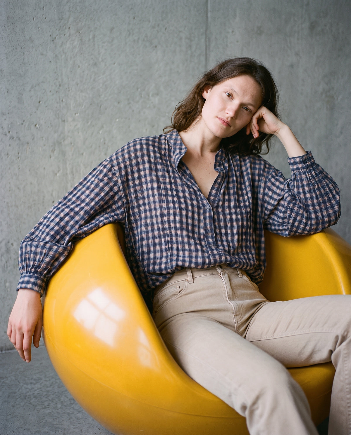 Brunette woman wearing a KIDDING relaxed navy and blush gingham check blouse with flared beige trousers.