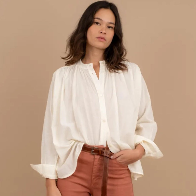 Woman wearing a beige blouse and brown pants against a beige background