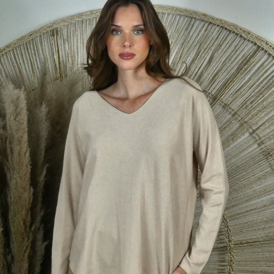 Woman wearing a beige long-sleeve top and brown pants against a neutral background