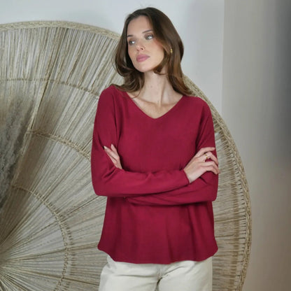 Woman wearing a wine V neck knit pants standing in front of a decorative wall piece.