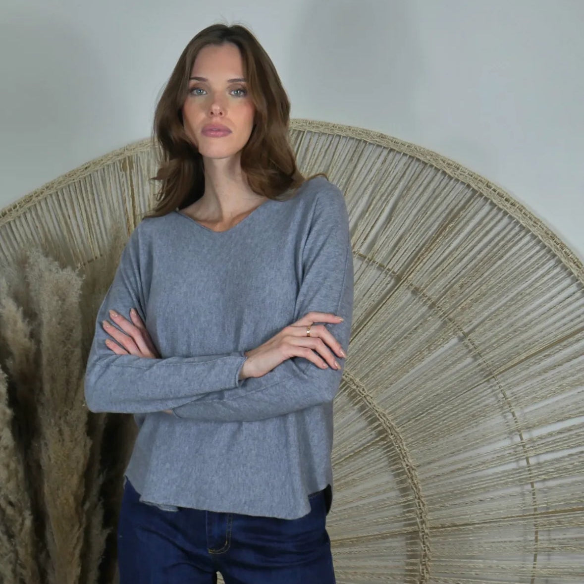 Woman wearing a gray sweater and blue jeans standing in front of a decorative wall piece.