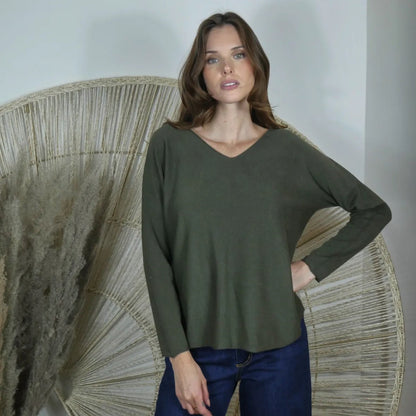 Woman wearing a green sweater and blue pants standing in front of a decorative fan.