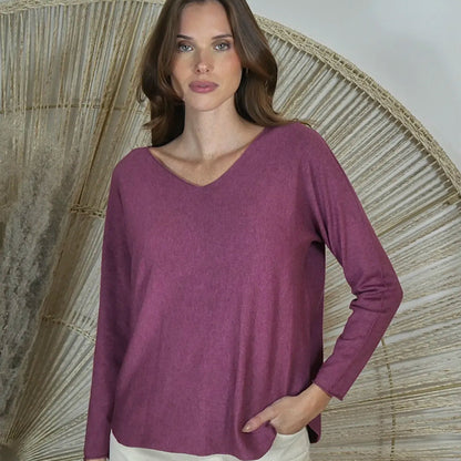 Woman wearing a purple long-sleeve top standing against a textured wall.