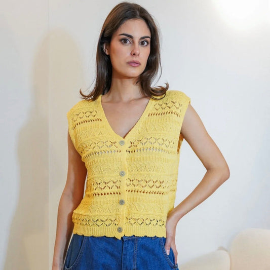 Woman wearing a yellow sleeveless crochet top with blue jeans indoors.