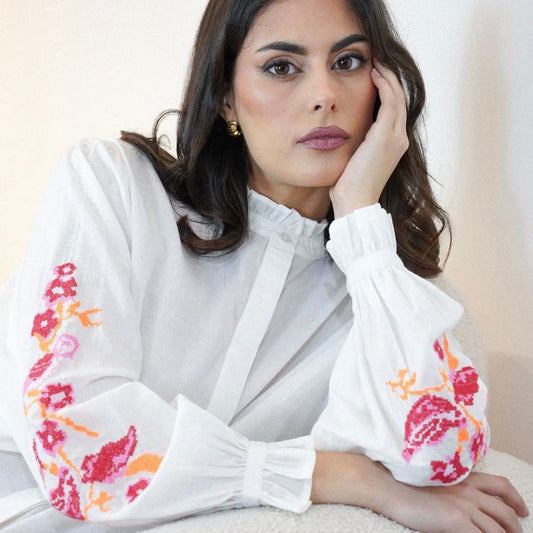 Woman wearing a white blouse with floral embroidery on a plain background