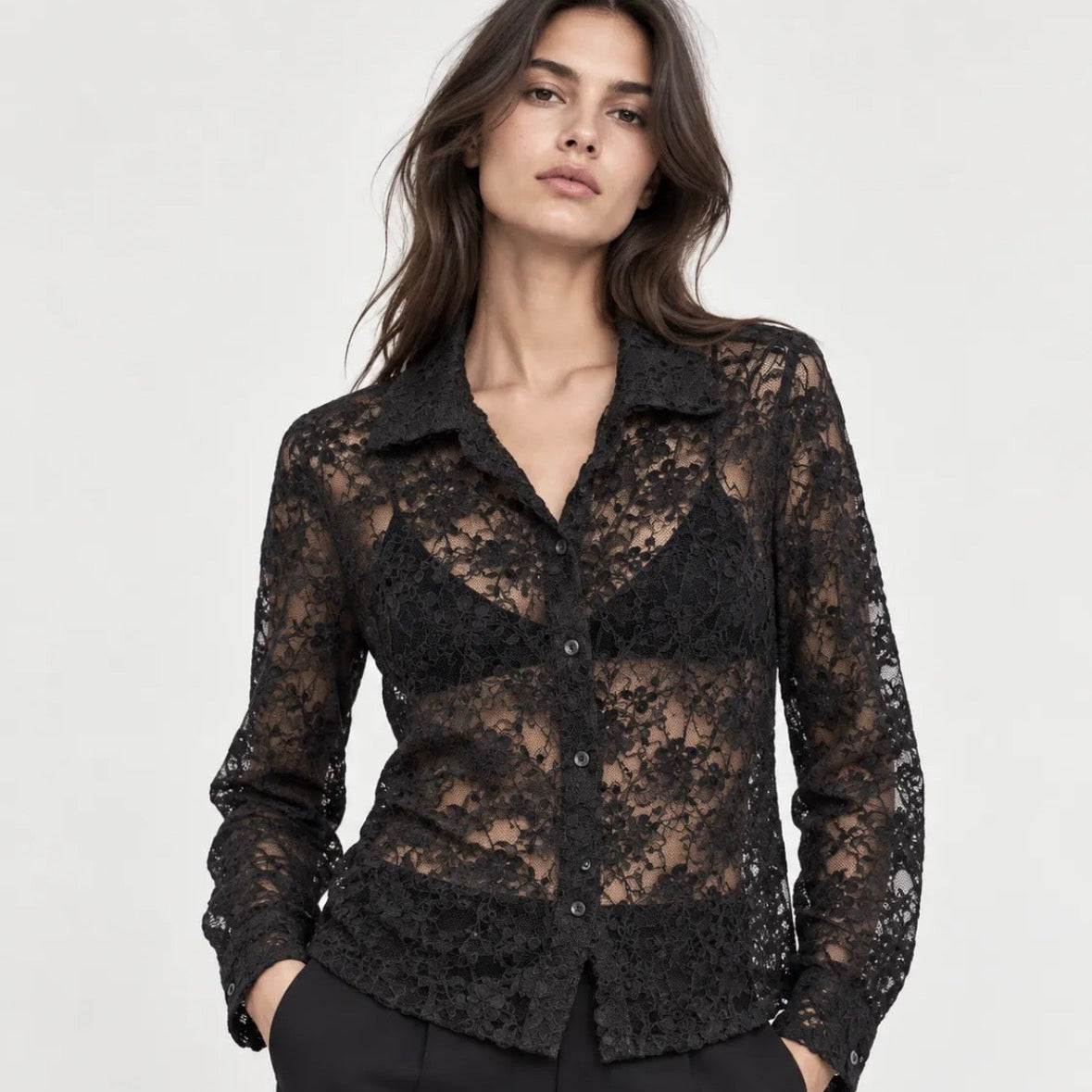 Woman wearing a sheer KIDDING black floral lace long-sleeve button-down shirt paired with tailored black trousers