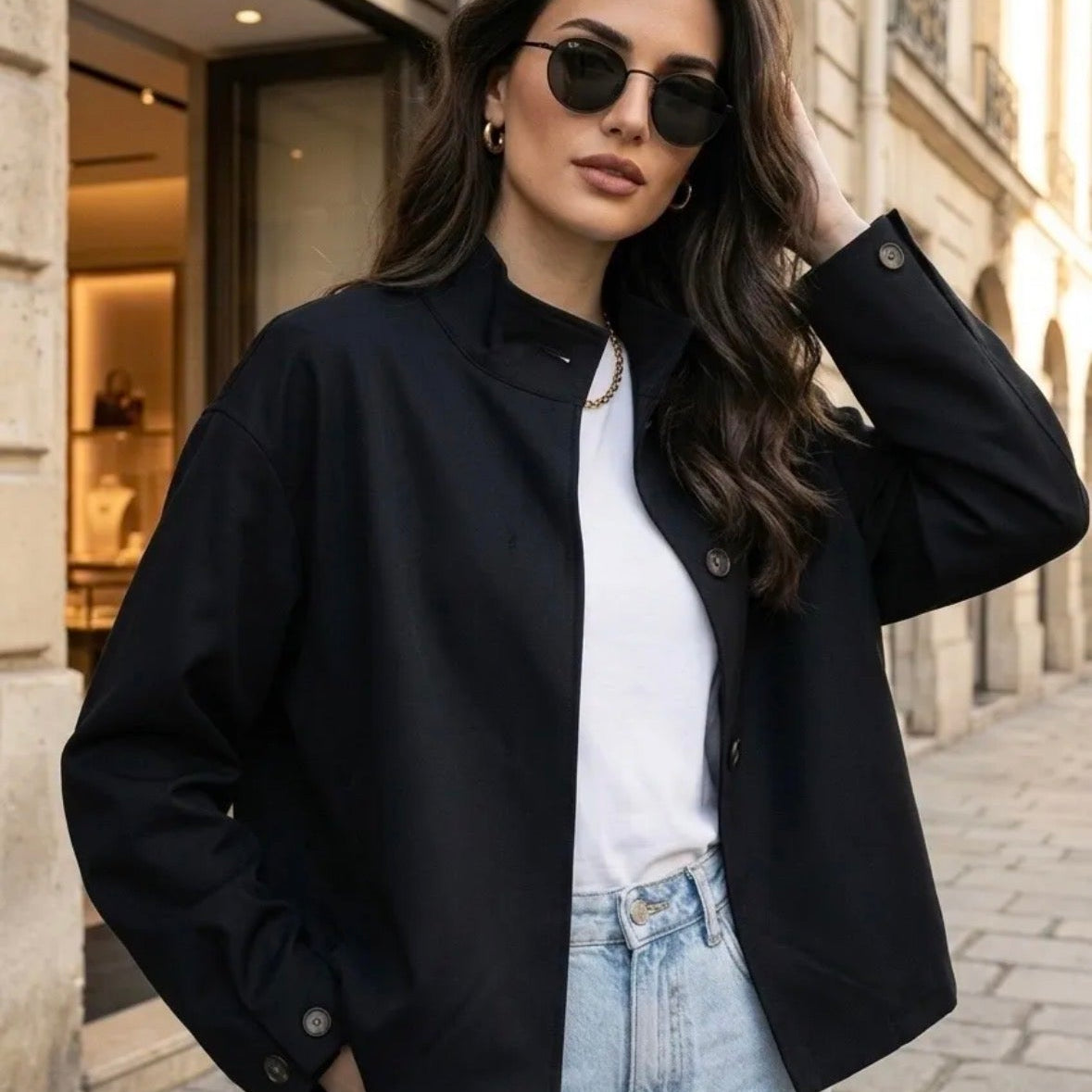 Model wearing KIDDING black stand-collar jacket with hidden front zip, angled welt pockets, paired with light-wash jeans and aviator sunglasses on a Paris street