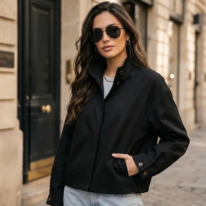 Model wearing KIDDING black stand-collar jacket with hidden front zip, angled welt pockets, paired with light-wash jeans and aviator sunglasses on a Paris street