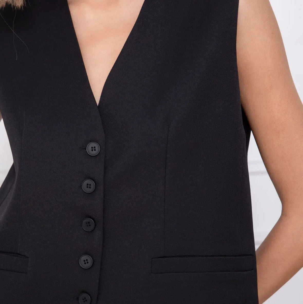 Model wearing KIDDING black tailored suiting vest as a standalone top with matching trousers, gold necklace, and sunglasses