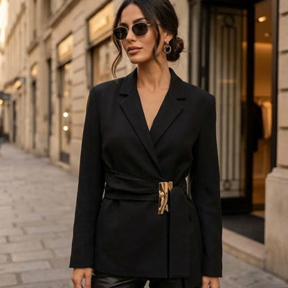 Model wearing KIDDING black tailored wrap blazer with notched lapels, structured shoulders, and self-tie waist belt with sculpted gold metal buckle paired with black leather pants