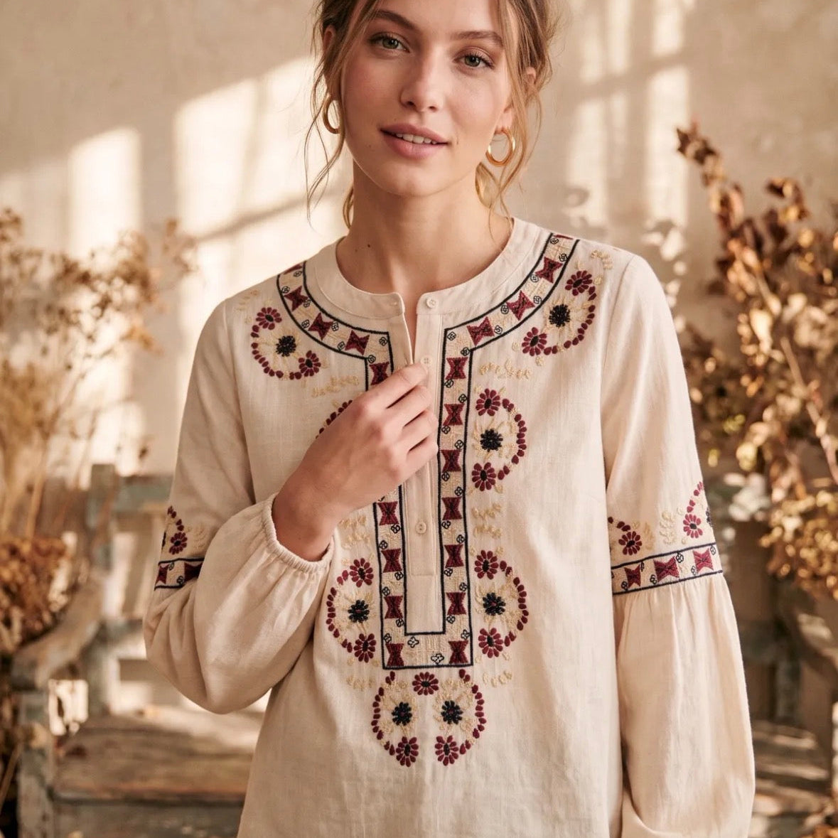 Model wearing KIDDING ecru cotton tunic blouse with burgundy and navy geometric folk embroidery, split button collar, and long balloon sleeves