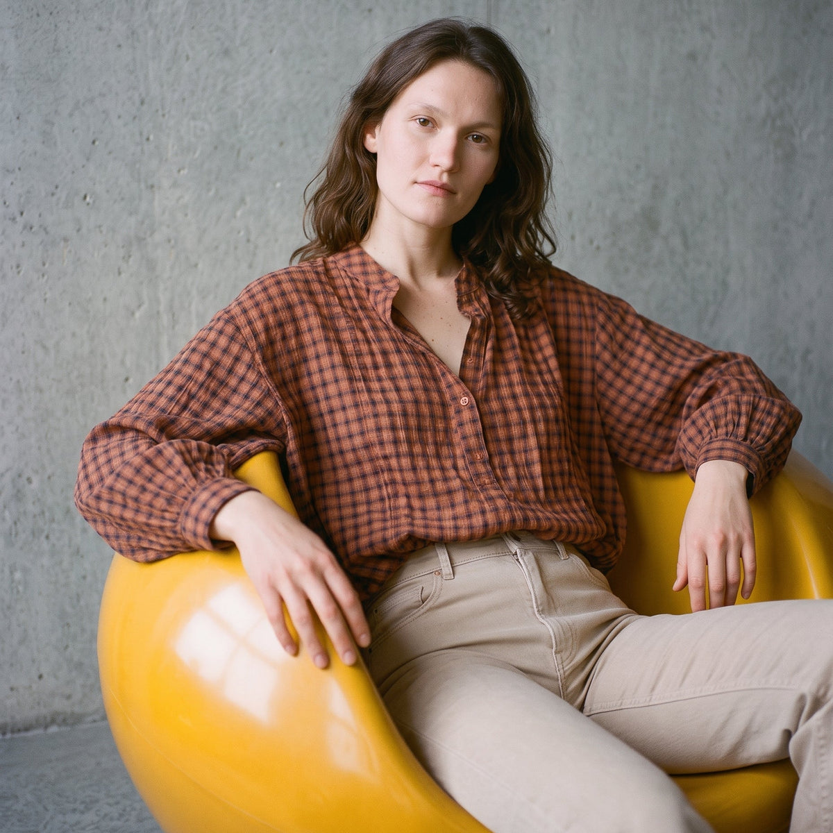 Woman wearing a KIDDING terracotta and brown gingham gathered blouse tucked into beige high-waisted jeans