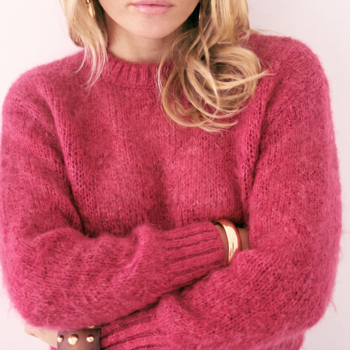 Close-up of a blonde woman wearing a KIDDING vibrant raspberry pink alpaca-blend crewneck JUMPER with ribbed cuffs and statement black sunglasses.