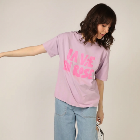 Person wearing a pink t-shirt with text and light blue jeans on a plain background
