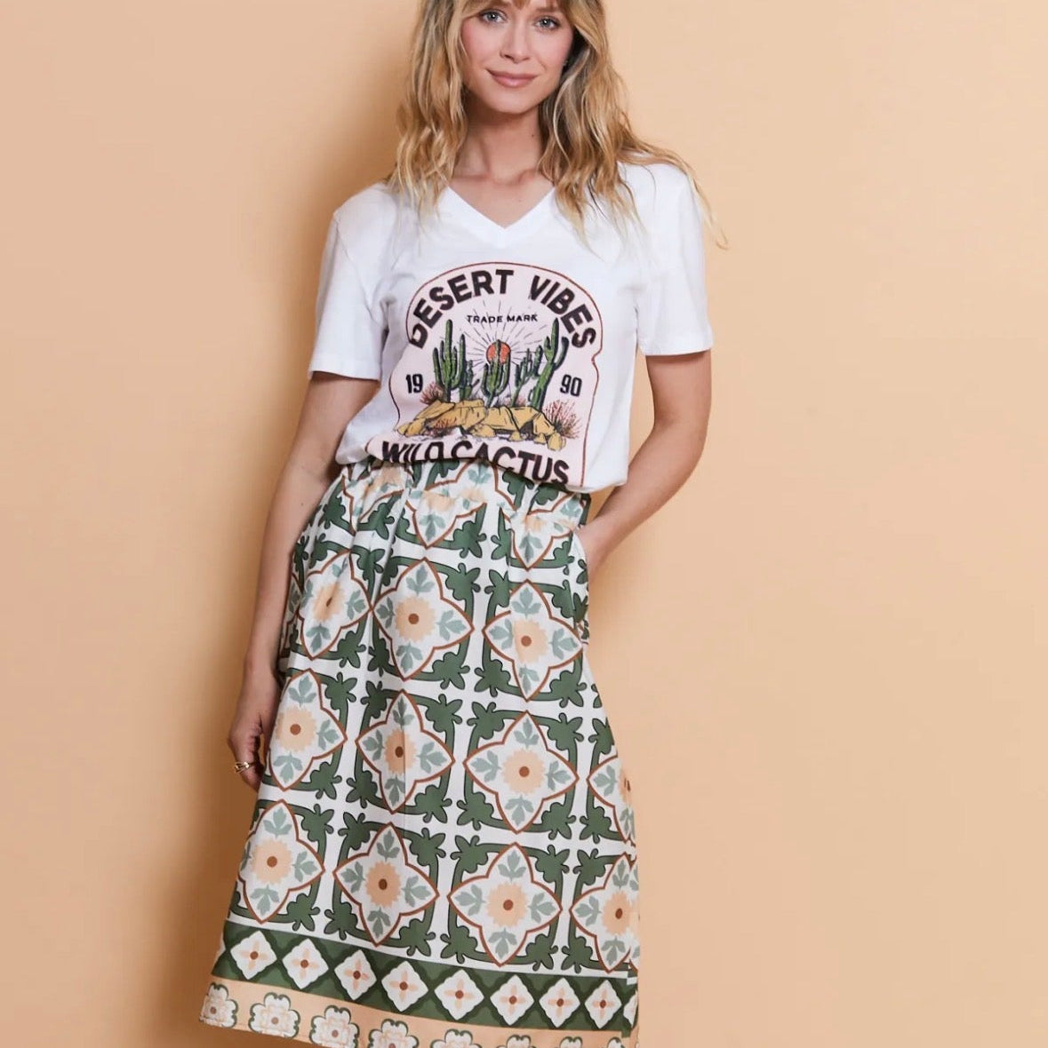 Woman wearing a white t-shirt with cactus design and a patterned skirt on a beige background