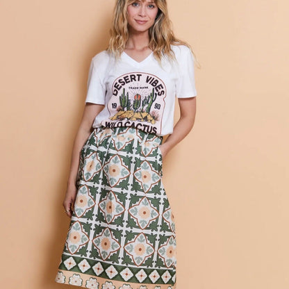 Woman wearing a white t-shirt with cactus design and a patterned skirt on a beige background
