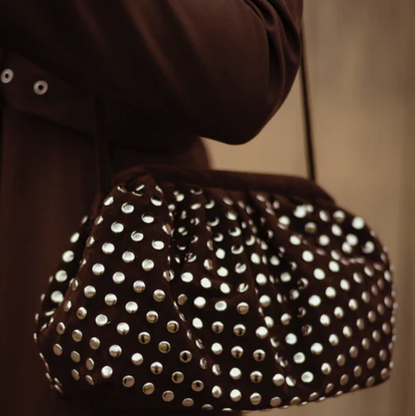 brown handbag with silver studs held by a person wearing a brown coat.