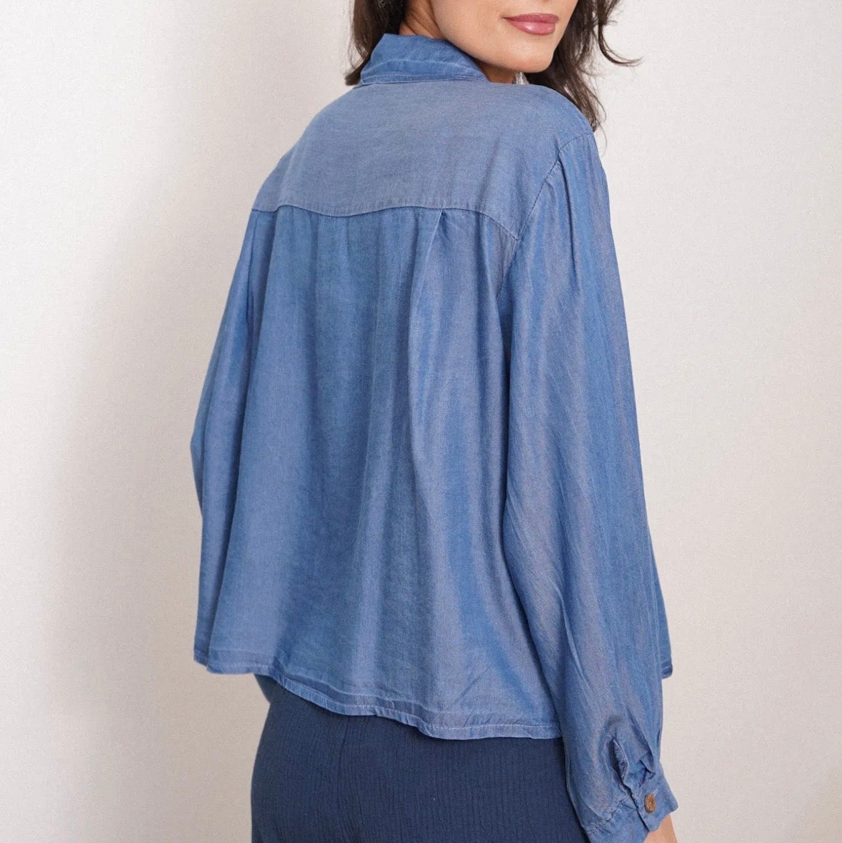 Woman wearing a blue denim shirt against a plain background