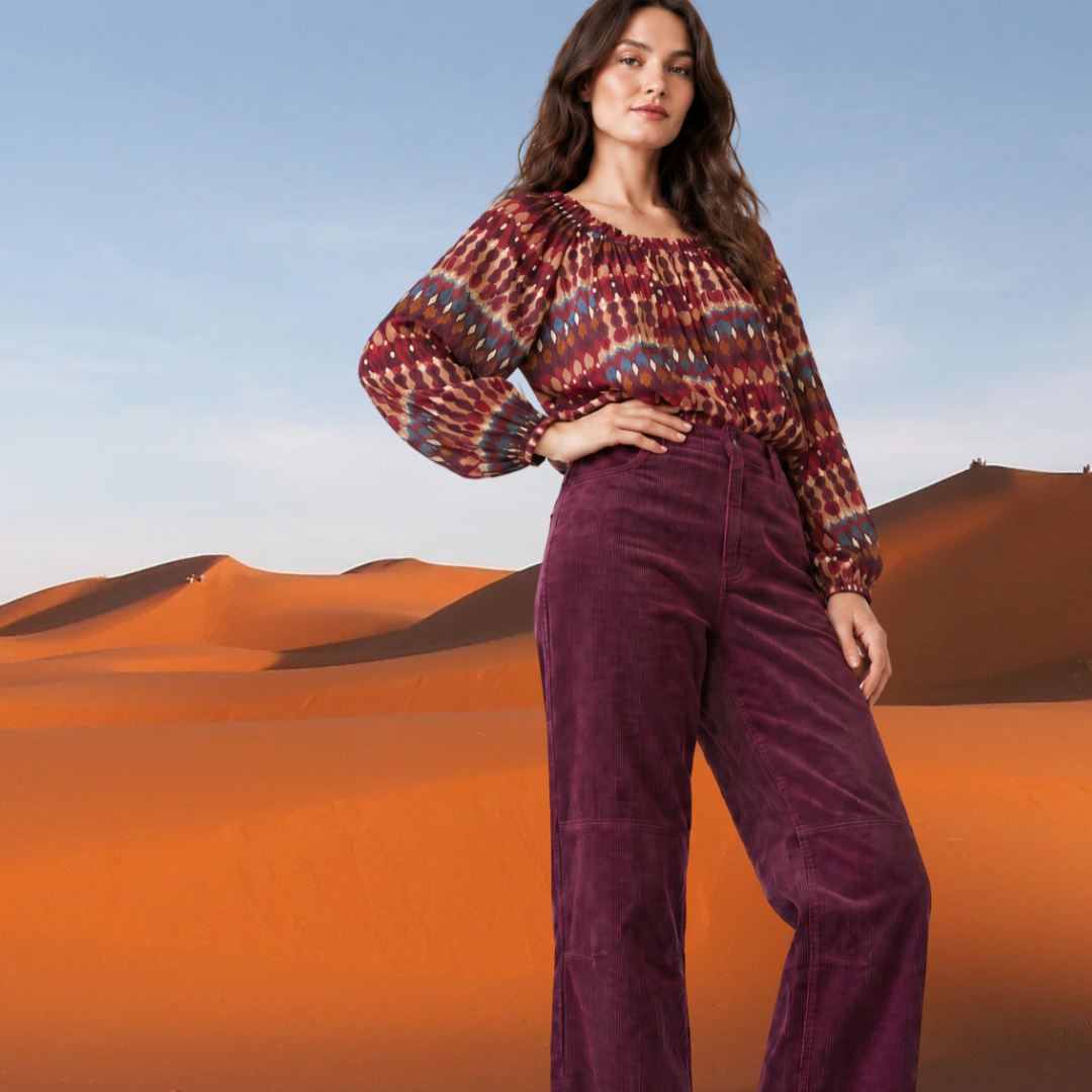 Woman modeling a kidding bohemian long-sleeve blouse with a gathered scoop neckline and billowy sleeves in a burgundy, rust, and teal geometric pattern.