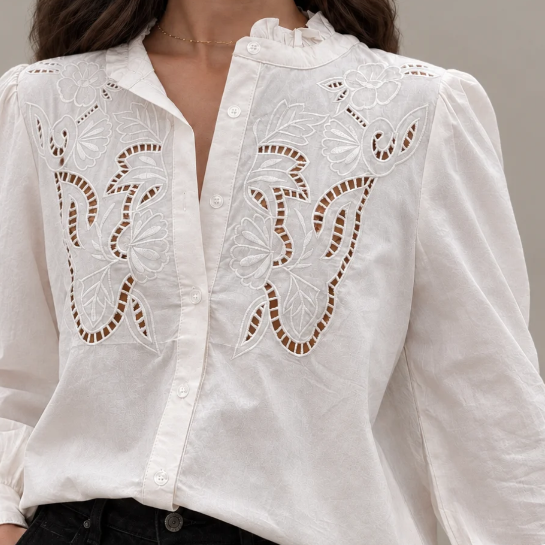 Close-up of a woman wearing a kidding white long-sleeve button-up blouse featuring symmetric floral cutwork embroidery and a ruffled stand collar, tucked into black pant.